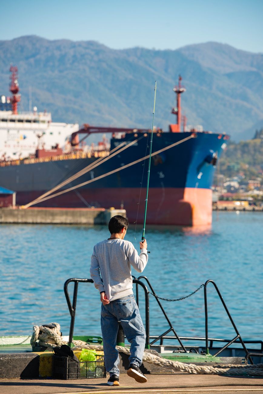 fisherman at harbor with cargo ship in background